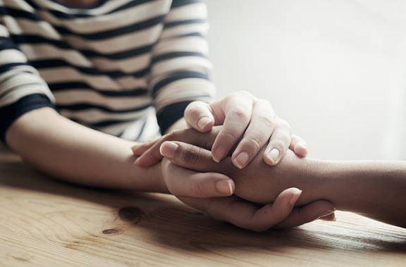 Image shows two people's hands and arms and they are holding hands in support