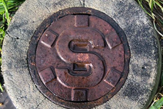 Sewer shaft with metal lid surrounded by concrete