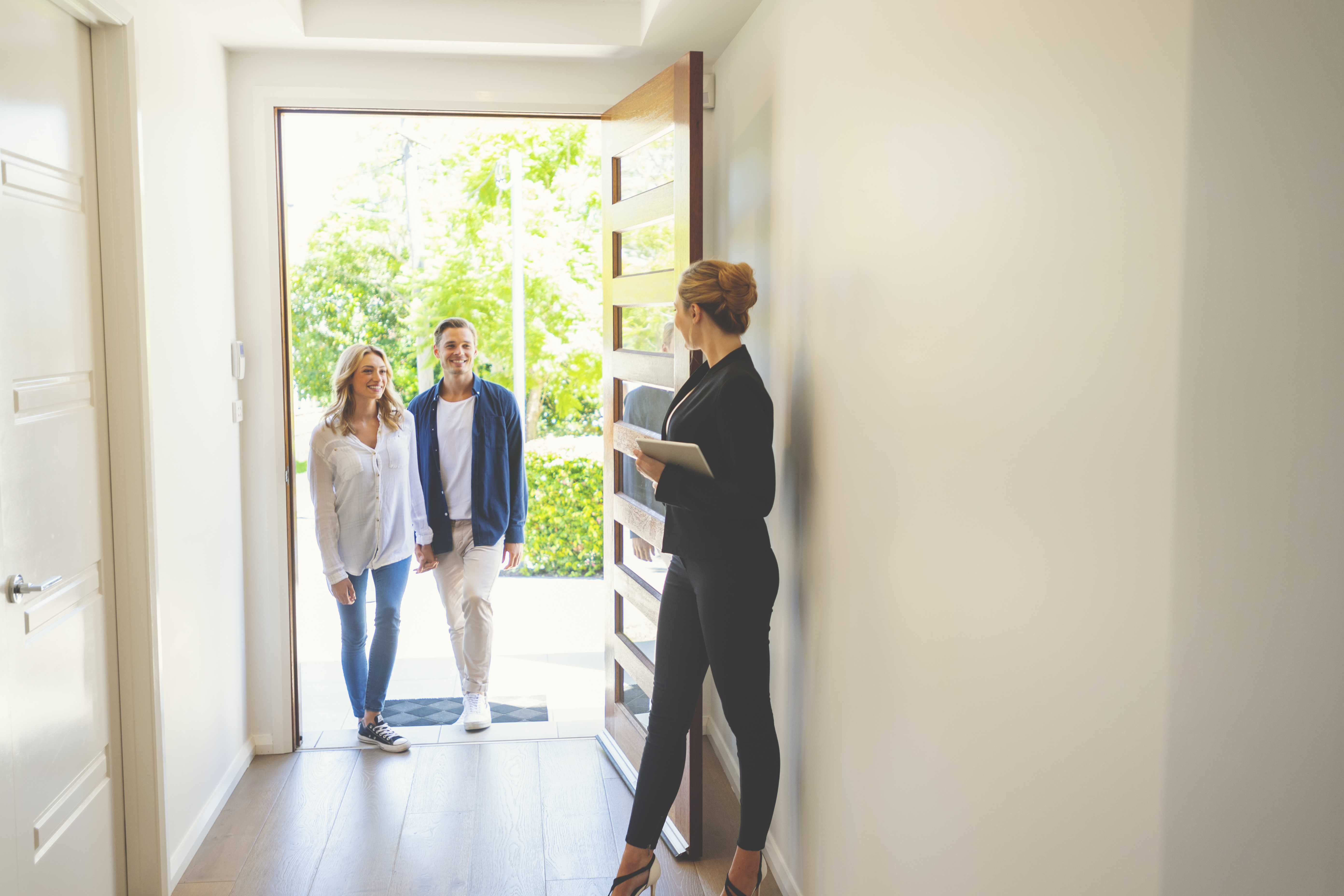 woman and man stand outside an open front door held by a woman holding a notebook